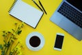 Smartphone and note, flowers, coffee, laptop on yellow background. Office concept .