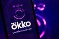 Smartphone with okko online movie theater logo on screen.