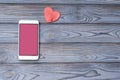 Smartphone with a pink screen, heart shape on a wooden background.