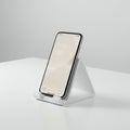 A smartphone with a sleek design rests on a white triangular stand atop a smooth w