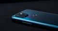 A smartphone with a sleek gradient blue finish lies on a flat black surface. The back