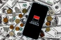 Smartphone with Societe Generale bank logo surrounded by variety of metal coins on background of dollar bills Royalty Free Stock Photo