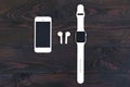 Smartphone, sports watch with a white strap, band, wireless headphones bluetooth on a dark wooden background.