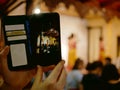A smartphone on a tourist`s hands taking a photograph of Northern Thai dancing performing on a stage