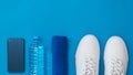 Smartphone, water bottle, towel and white sports shoes on blue background. Sports style. Flat lay.