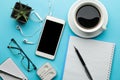 Smartphone. White phone and a cup of coffee and a notebook with glasses on a bright light blue background. top view Royalty Free Stock Photo