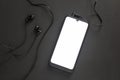 A smartphone with a white screen lies on a black background with stuck headphones Royalty Free Stock Photo