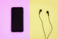 Smartphone and Wired earphones on pink and yellow background Royalty Free Stock Photo