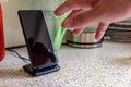 Smartphone wireless charging on charging stand on kitchen tabletop. male hand placing phone to charging