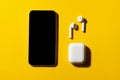 Smartphone and wireless headphones on yellow background.