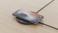 A smartphone is wirelessly charging on a circular pad on a wooden surface Royalty Free Stock Photo
