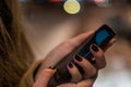 Smartphone in woman hands in front of blurred city lights