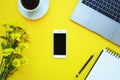 Smartphone on yellow background with note, flowers, coffee and laptop