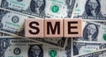 SME concept. Word `SME - small and medium-sized enterprises` on cubes on a beautiful background from dollar bills. Business and