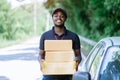 Smile african man postal delivery courier man in front of car delivering package Royalty Free Stock Photo