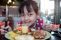 Smile asian child girl eating steak and vegetable salad on the table with holding knife and fork Royalty Free Stock Photo