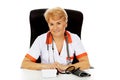 Smile elderly female doctor or nurse sitting behind the desk with bloog preasure gauge Royalty Free Stock Photo