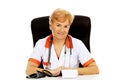 Smile elderly female doctor or nurse sitting behind the desk with bloog preasure gauge Royalty Free Stock Photo