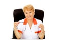 Smile elderly female doctor or nurse sitting behind the desk and holds two pair of glasses Royalty Free Stock Photo