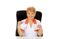 Smile elderly female doctor or nurse sitting behind the desk and holds two pair of glasses Royalty Free Stock Photo