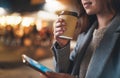 Smile girl drink coffee outdoors using mobile smartphone on background bokeh light in night city, womn hold in hands ecology Royalty Free Stock Photo