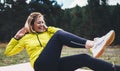 Smile girl exercising outdoors in green park, activity with stretch legs. Happy fitness woman laughing doing stretching exercises