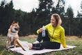 Smile girl with shiba inu dog together relax after exercising outdoors on yoga mat, pet on nature with fitness woman drink water