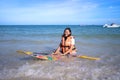Smile happy Asian woman with life-saving jacket sit on small paddleboard holding oar at wavy sea beach