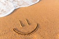 smile painted on the sand next to a foamy wave. Sandy beach with a friendly message written on it Royalty Free Stock Photo