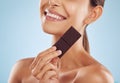 Smile, skincare and woman with chocolate for beauty isolated on a blue background. Happy, candy and model with food