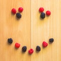 Smile symbol formed from raspberries and blackberries on a wooden background.
