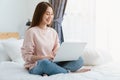 Smile young Asian woman sitting on bedroom in the morning and using laptop online on the Internet.