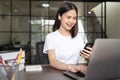 Smiley Asian woman hand holding smartphone and press the button on the keyboard laptop in house. Royalty Free Stock Photo