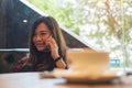 Asian woman sitting on sofa , using and talking on smart phone in modern cafe with coffee cup and wooden table foreground Royalty Free Stock Photo