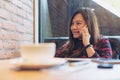 A smiley beautiful Asian woman sitting on sofa , using and talking on smart phone in modern cafe Royalty Free Stock Photo