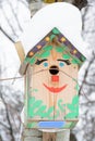 Smiley birdhouse. Birdhouse in the form of a funny face on the tree. Handmade wooden nesting box covered in snow. Winter landscape