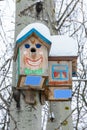 Smiley birdhouses. Birdhouse in the form of a funny face on the tree. Handmade wooden nesting box covered in snow. Winter landscap