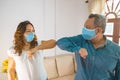 Smiley couple wearing protective face masks waving elbows in the workplace, co-workers wearing face covers protect themselves from