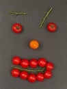 Smiley face with a surprised expression. Laying out parts of a human face with vegetables, namely tomatoes and tomato branches