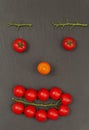 Smiley face with a surprised expression. Laying out parts of a human face with vegetables, namely tomatoes and tomato branches