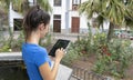 Smiley Lady sitting in a stone fountain relaxing with portable device downloading from internet. Teen student with dark hair