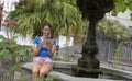 Smiley Lady sitting in a stone fountain relaxing with portable device downloading from internet. Teen student with dark hair