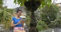 Smiley Lady sitting in a stone fountain relaxing with portable device downloading from internet. Teen student with dark hair