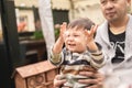 Smiley male infant raising his hands in excitement sitting on his father's legs, dad is holding baby with his hands. Royalty Free Stock Photo