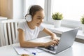 Smiley teenager girl doing homework at home in front of a laptop monitor