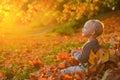 Smilimg cute little girl sitting on the covered leaves watching the leaves fall. Autumn dream. Kid dreams on autumn