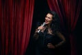 Smiling woman singer sing with microphone over Red Curtain Performing on stage, spotlights, Woman Royalty Free Stock Photo