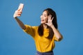 Smiling adorable Asian female making selfie photo on smart phone with positive expression in casual clothing and stand isolated on Royalty Free Stock Photo