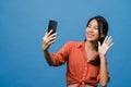 Smiling adorable Asian female making selfie photo on smart phone with positive expression in casual clothing and stand isolated on Royalty Free Stock Photo