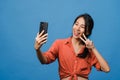 Smiling adorable Asian female making selfie photo on smart phone with positive expression in casual clothing and stand isolated on Royalty Free Stock Photo